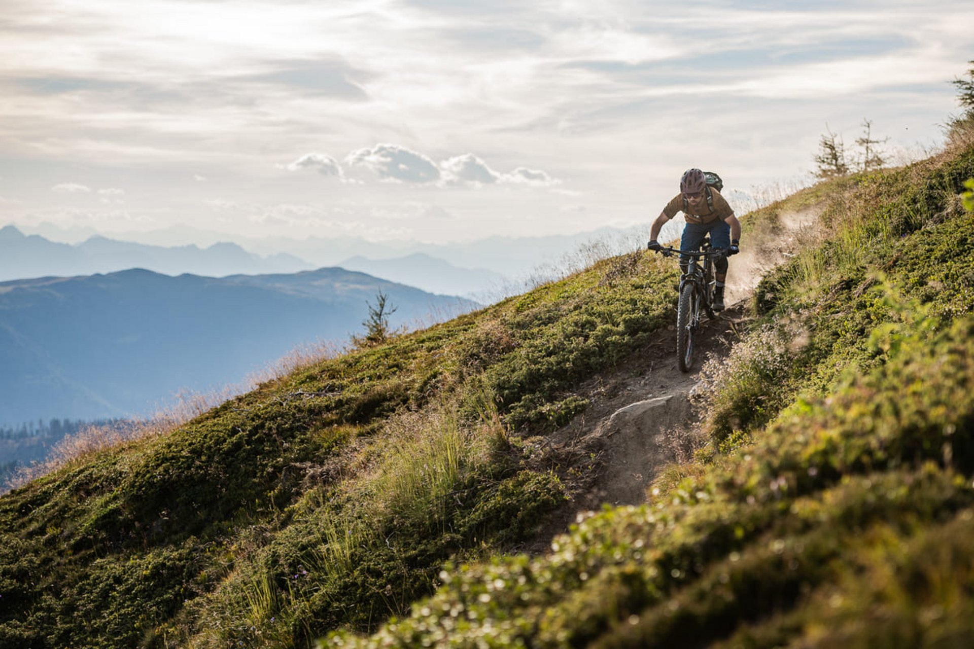 Mountain biker riding downhill on narrow trail in mountain landscape