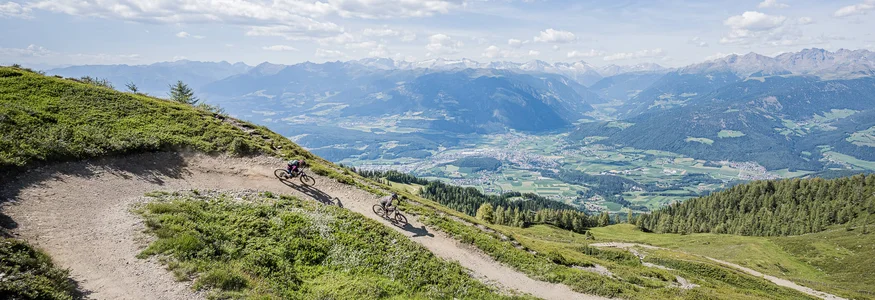 Zwei Mountainbiker fahren auf einem Bergpfad mit Alpenpanorama