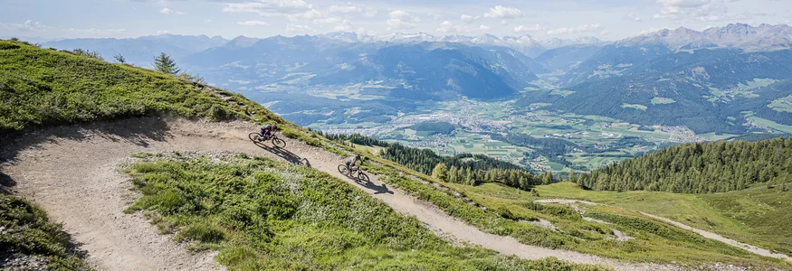 Zwei Mountainbiker fahren auf einem Bergpfad mit Alpenpanorama