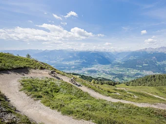 Two mountain bikers on a trail with alpine mountain view