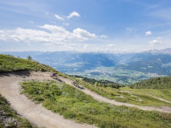 Two mountain bikers on a trail with alpine mountain view