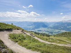 Zwei Mountainbiker fahren auf einem Bergpfad mit Alpenpanorama