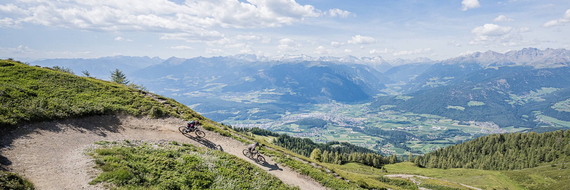 Zwei Mountainbiker fahren auf einem Bergpfad mit Alpenpanorama