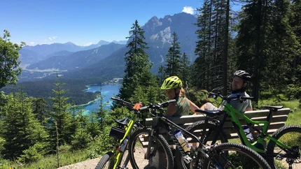 Zwei Radfahrer auf Bank mit Blick auf Berg und See in Alpen