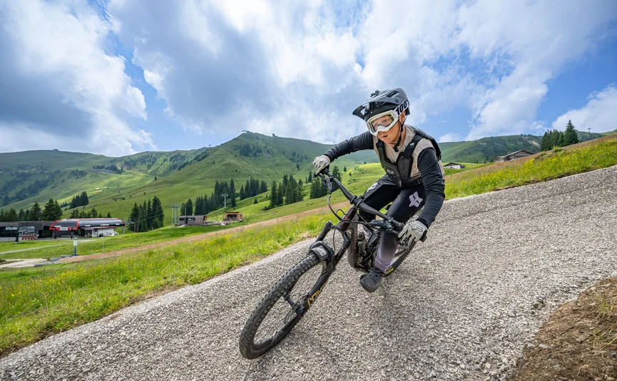 Mountainbiker fährt auf Schotterweg in grüner Berglandschaft bei bewölktem Himmel