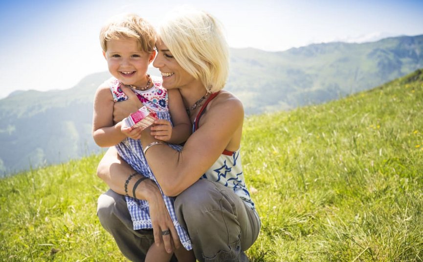 Moeder omhelst lachend kind op een weide met bergen op de achtergrond