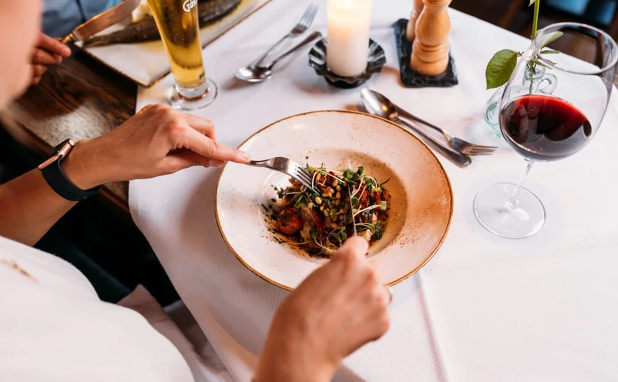 Person eating shrimp dish at elegant restaurant table with wine and beer