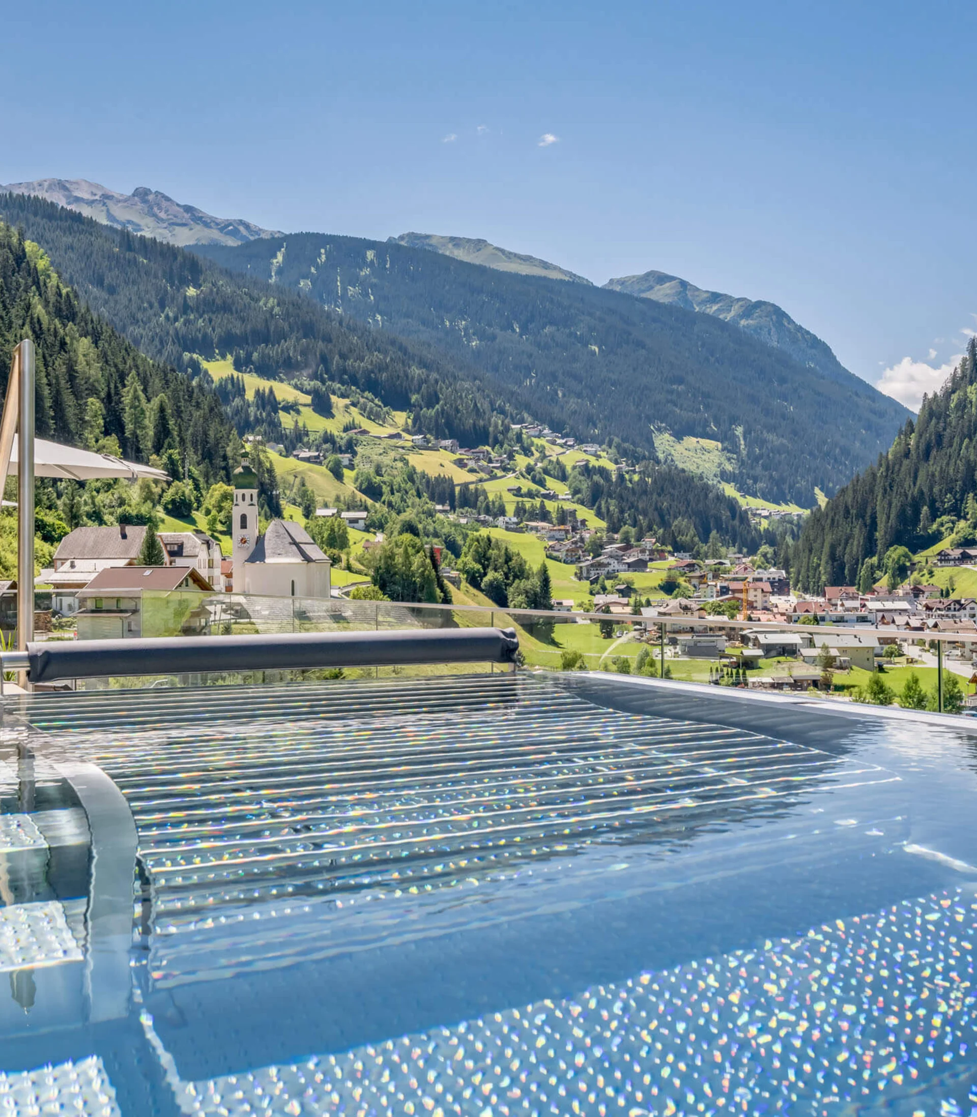 Infinity-Pool mit Blick auf ein Tal und bewaldete Berge unter blauem Himmel