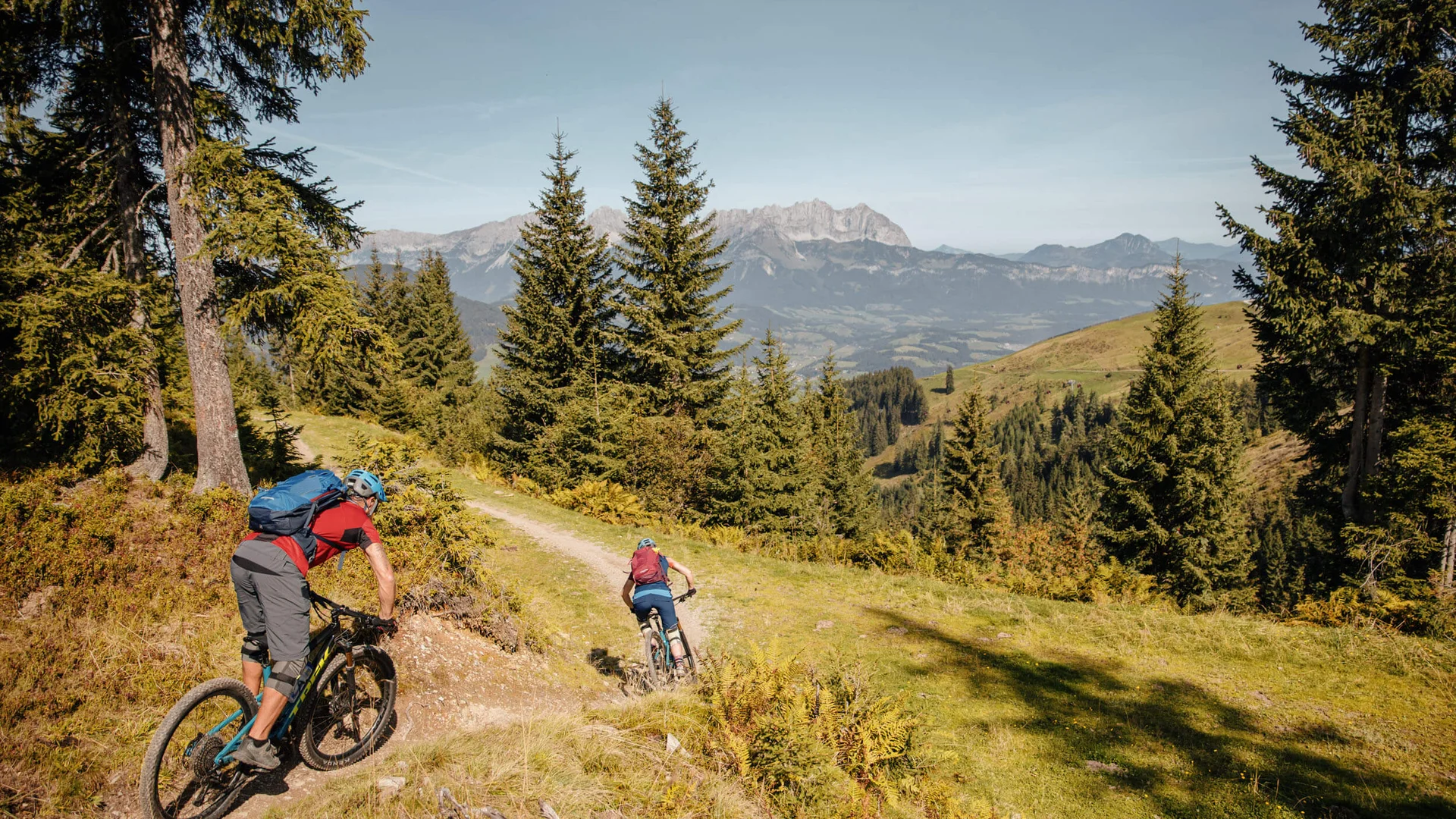 Zwei Mountainbiker auf Waldpfad mit Bergpanorama im Hintergrund
