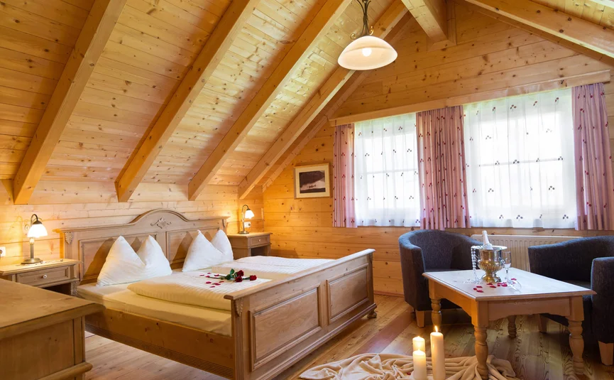 Knusse houten slaapkamer met tweepersoonsbed, kaarsen en champagne in landelijke stijl