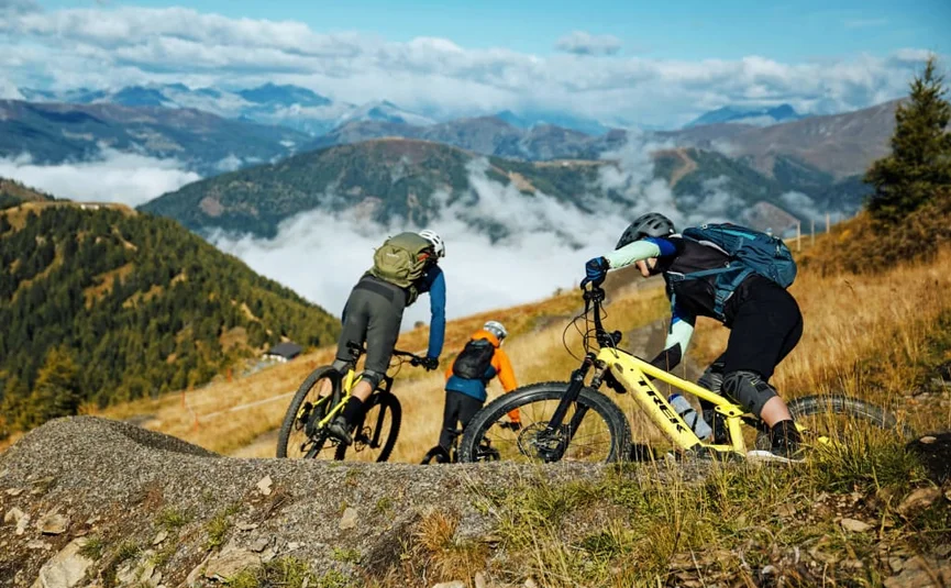Three mountain bikers on a trail with fog and mountain scenery
