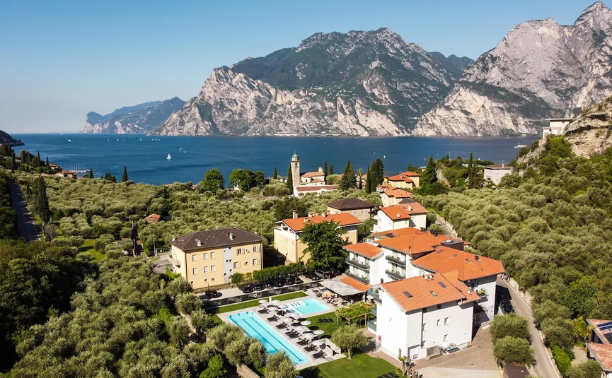 Village with pool, olive trees, and mountains by the lakeshore