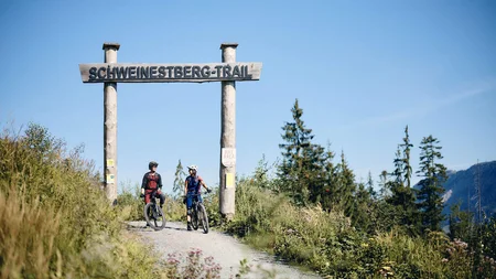 Unterwegs in Österreichs größter Bikeregion © Tobias Köhler Zwei Mountainbiker unter dem Schild Schweinestberg-Trail auf einem Waldweg