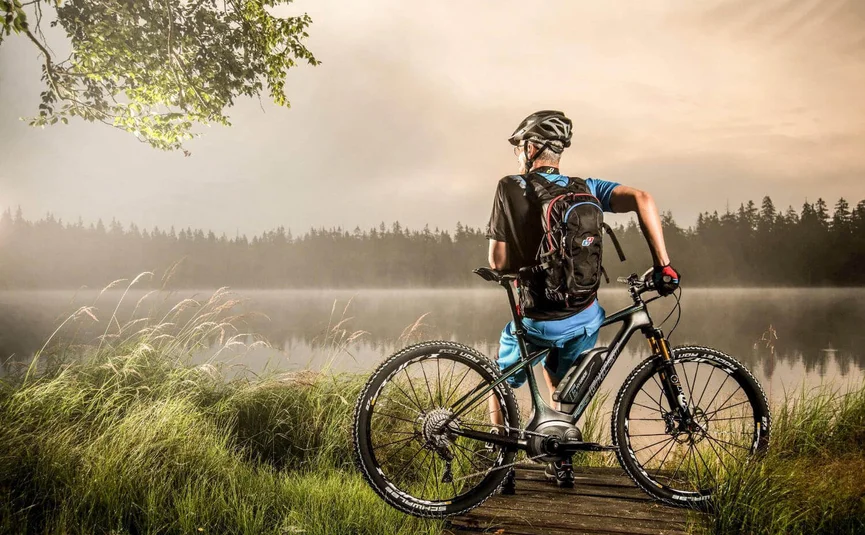 Radfahrer mit Helm und Rucksack blickt auf nebligen See und Wald