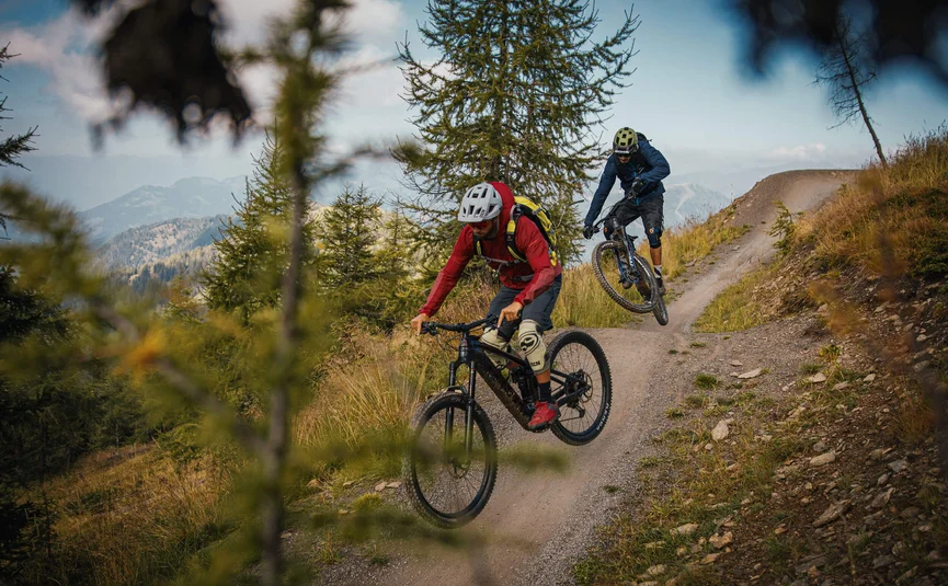 Two mountain bikers riding on a trail in a mountainous forest