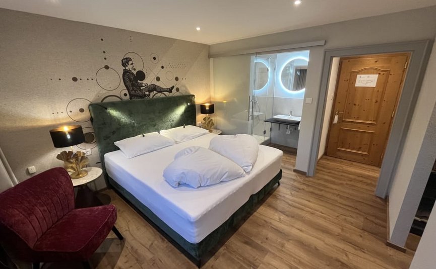 Modern eingerichtetes Hotelzimmer mit Doppelbett, Wandkunst und beleuchtetem Bad