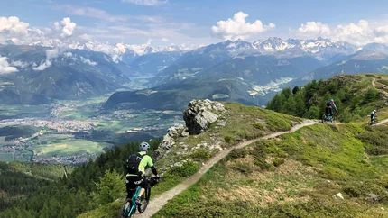 Mountain bikers riding trail with view of Alps and valley below