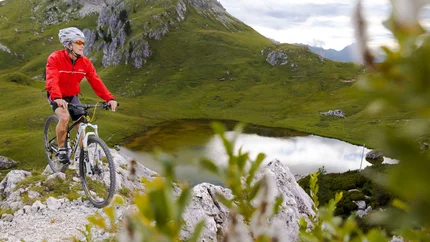Man mountain biking on rocky trail near lake and green hills