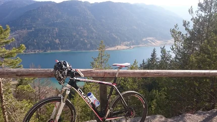 Mountainbike vor Bergsee und bewaldeten Bergen bei Sonnenschein