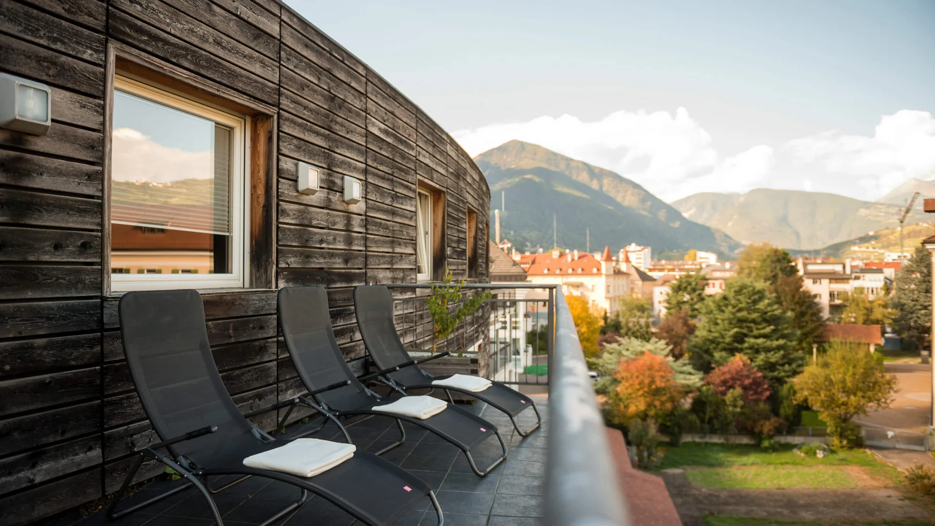 Balkon mit drei Liegestühlen vor Holzwand und Bergblick