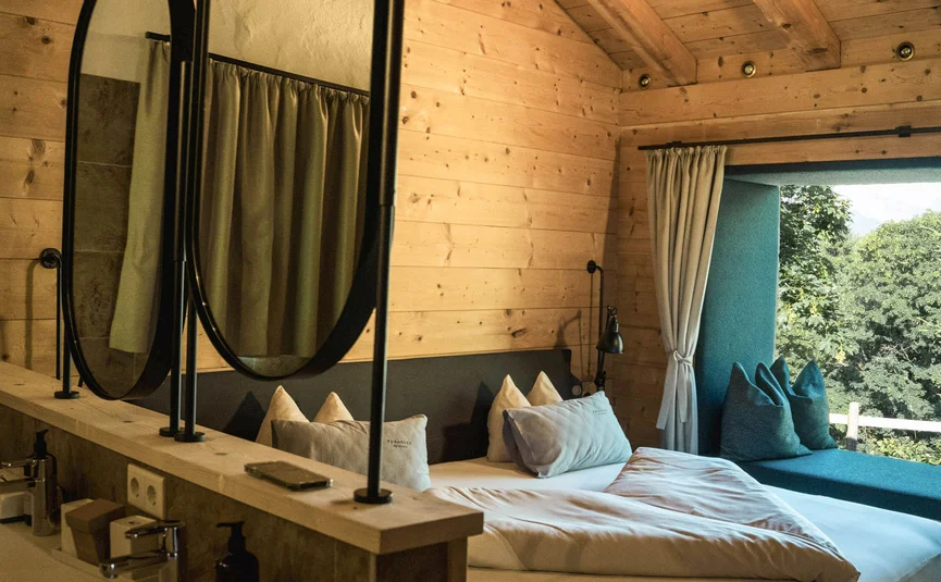 Gemütliches Schlafzimmer mit Holzwänden, Doppelbett und Fensterblick auf Bäume