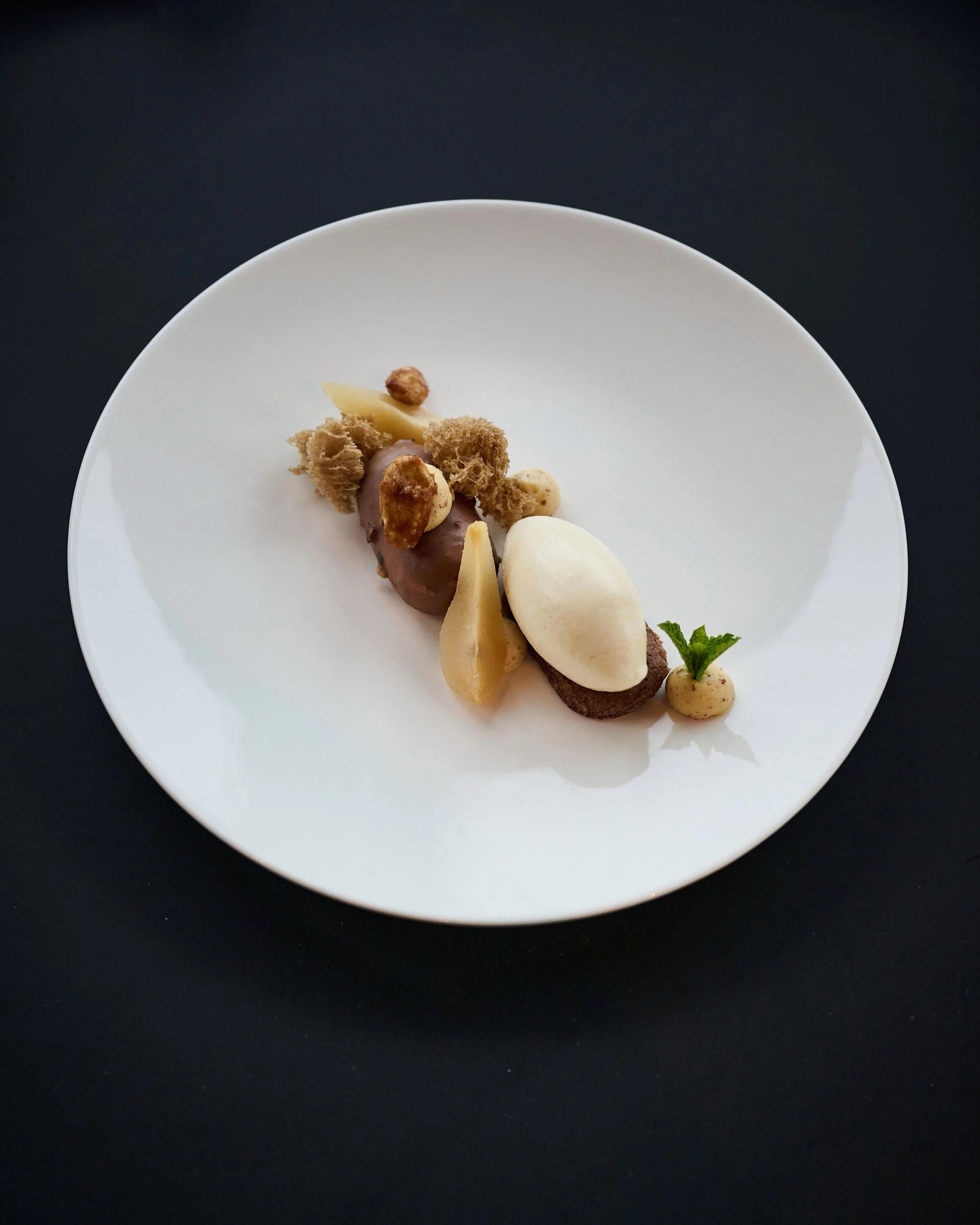 Fein angerichtetes Dessert mit Eis, Birne und Nüssen auf weißem Teller