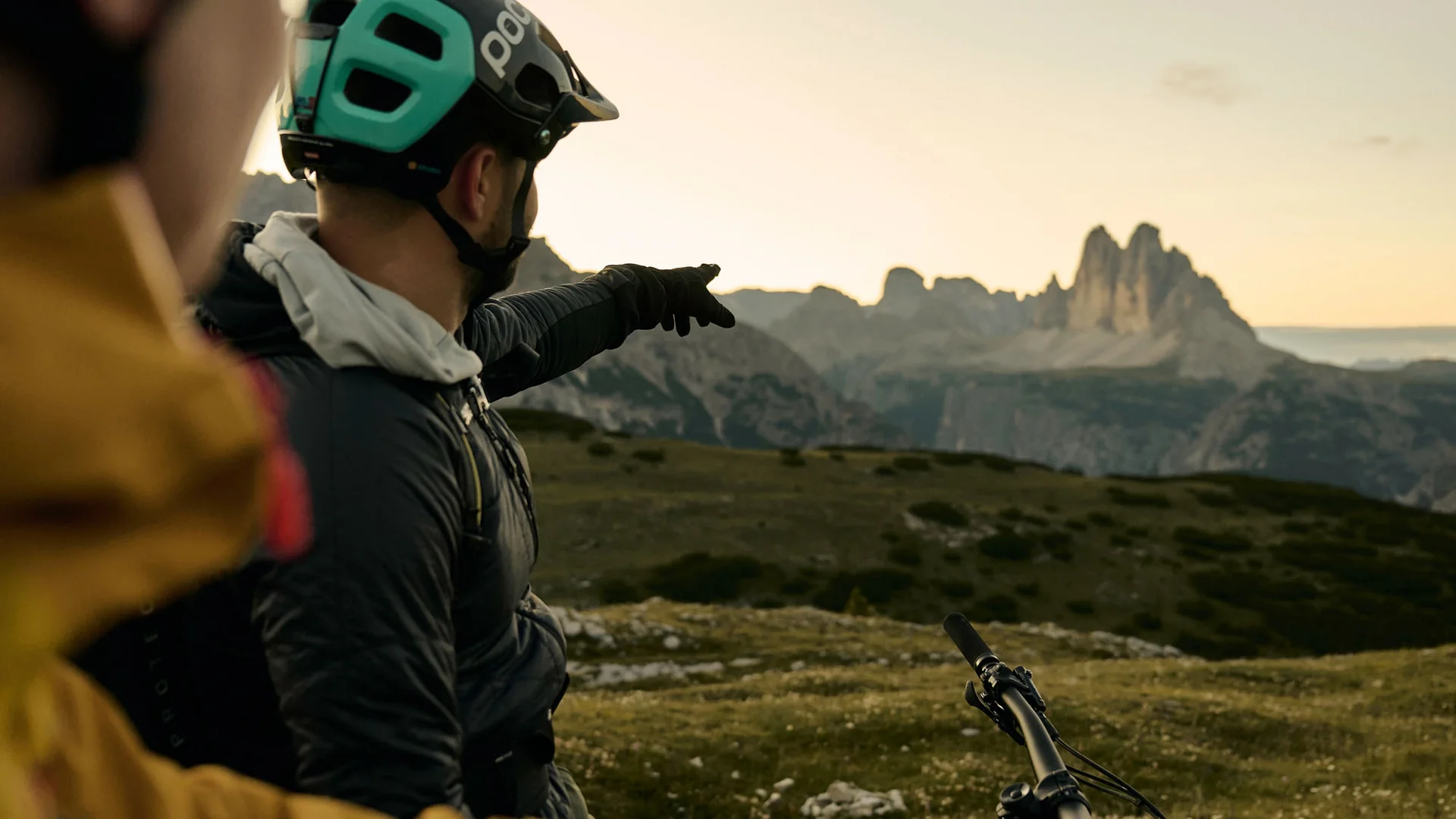 Zwei Mountainbiker mit Helmen schauen auf Berglandschaft bei Sonnenuntergang