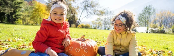 Zwei Mädchen sitzen im Park im Herbst neben Kürbis mit Herzen