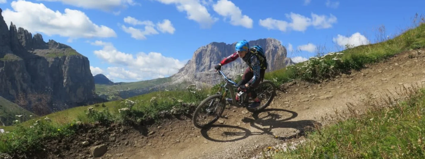 Dolomiten Active for Kids Mountainbiker fährt auf einem Bergweg mit Bergen und blauem Himmel im Hintergrund