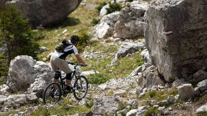 Mountainbiker fährt auf felsigem Bergpfad mit Markierung am Felsen