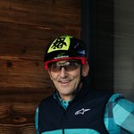 Radfahrer mit Helm und Handschuhen zeigt Daumen vor beleuchtetem G auf Holzwand