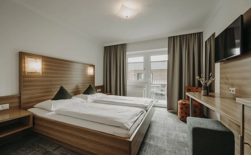 Modern hotel room with double bed, TV, and balcony