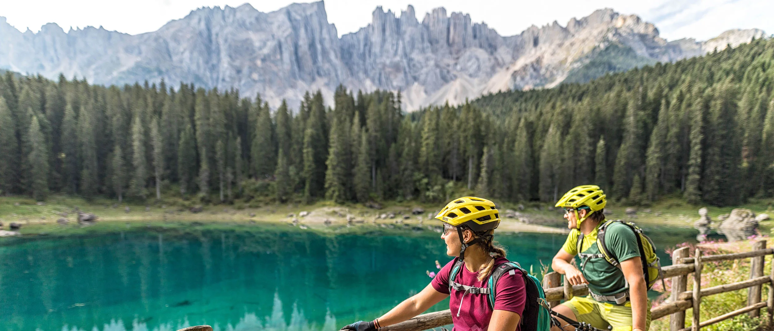 Two cyclists on mountain trail overlooking lake and mountains