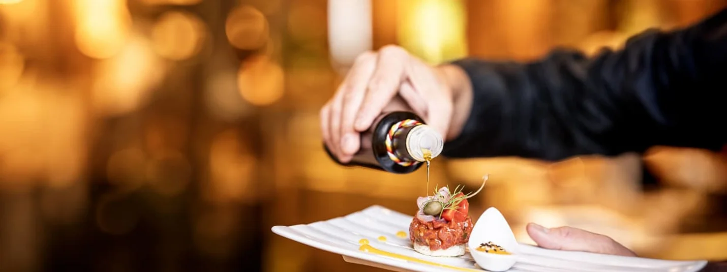 Hand giet olie over een kunstig opgediend gerecht op een wit bord