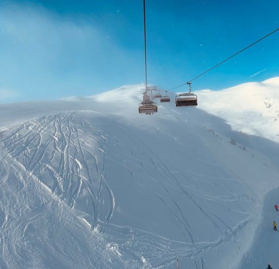 Skilift und Skifahrer auf verschneitem Berg unter blauem Himmel