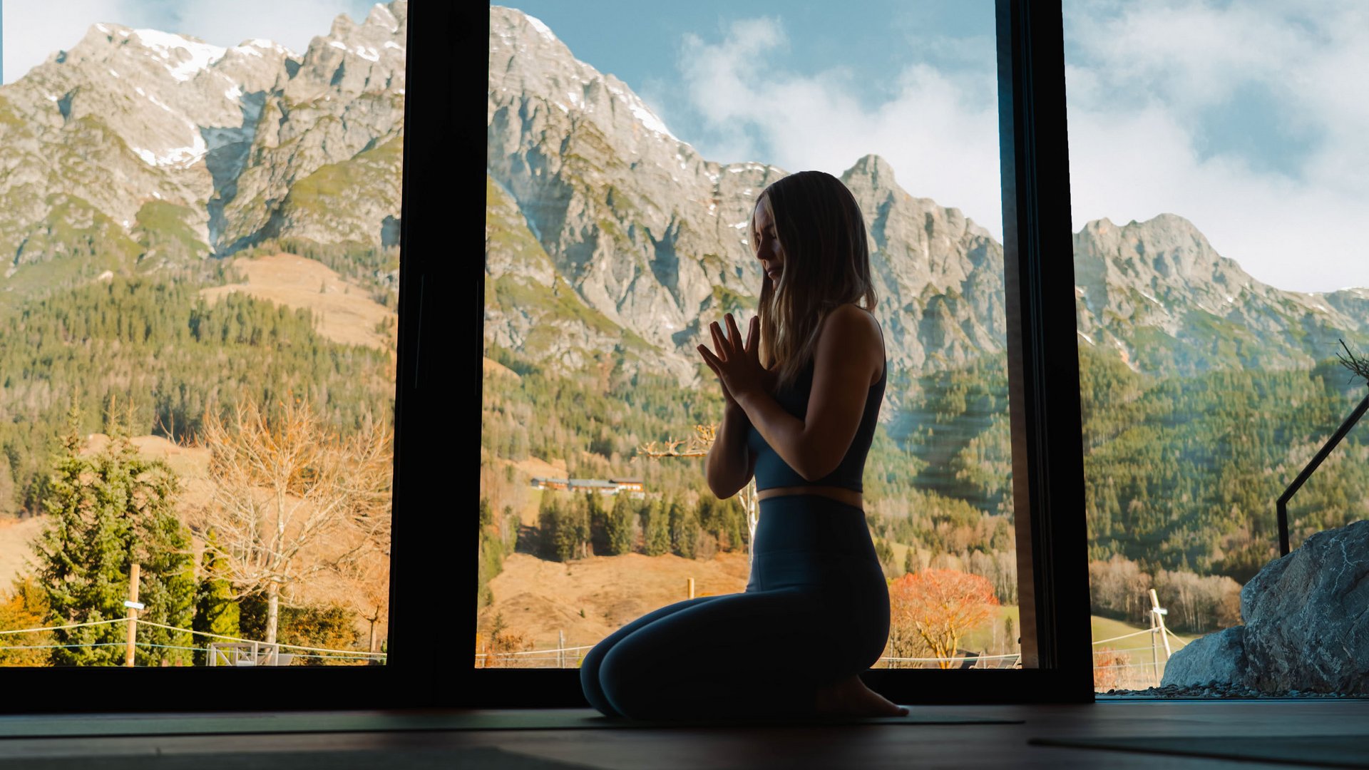 Frau meditiert drinnen mit Bergblick durch großes Fenster