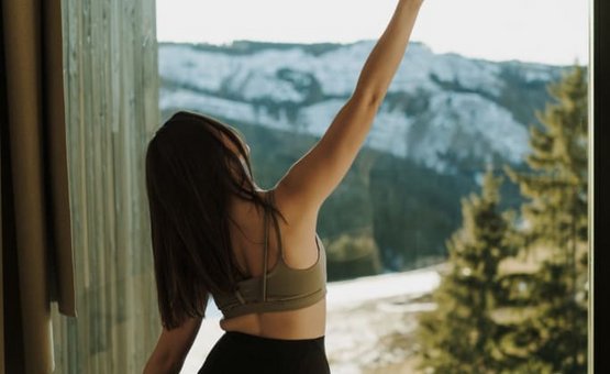 Frau macht Yoga mit Bergblick durch großes Fenster