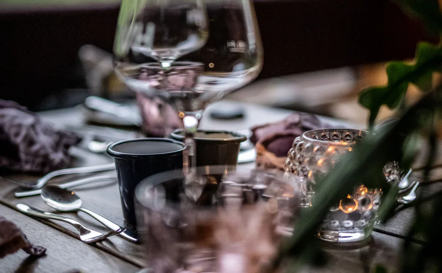 Gedeckter Esstisch mit Gläsern und Kerze vor grünem Hintergrund