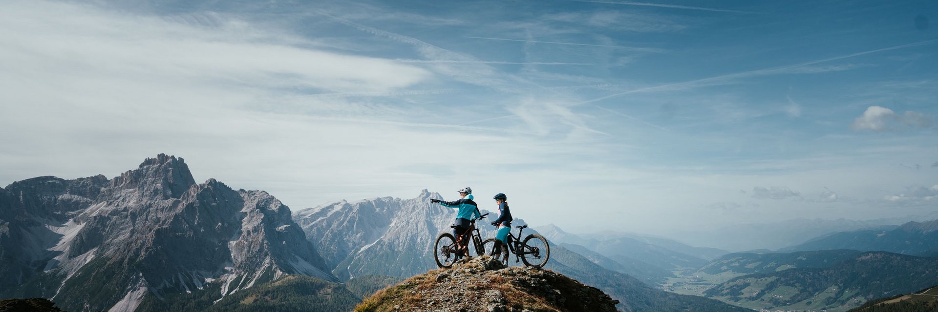 Zwei Mountainbiker auf einem Berggipfel mit Ausblick auf Gebirge