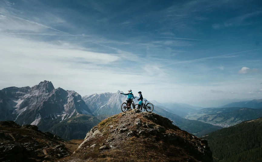 Zwei Mountainbiker auf einem Berggipfel mit Ausblick auf Gebirge
