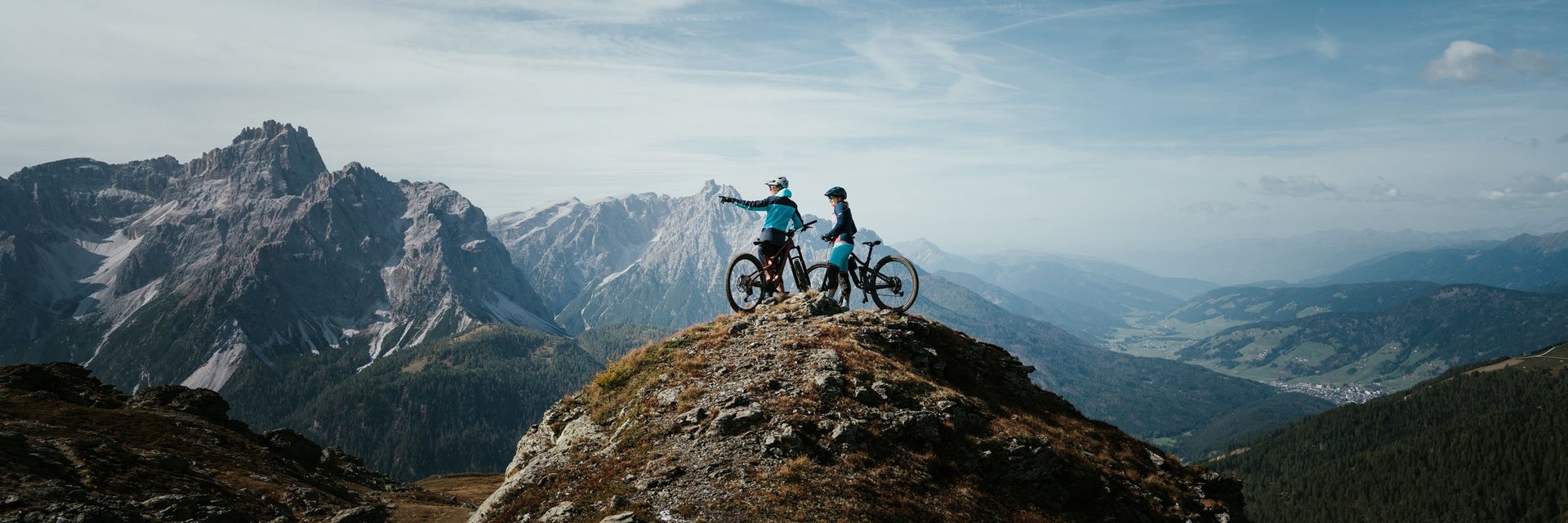 Zwei Mountainbiker auf einem Berggipfel mit Ausblick auf Gebirge