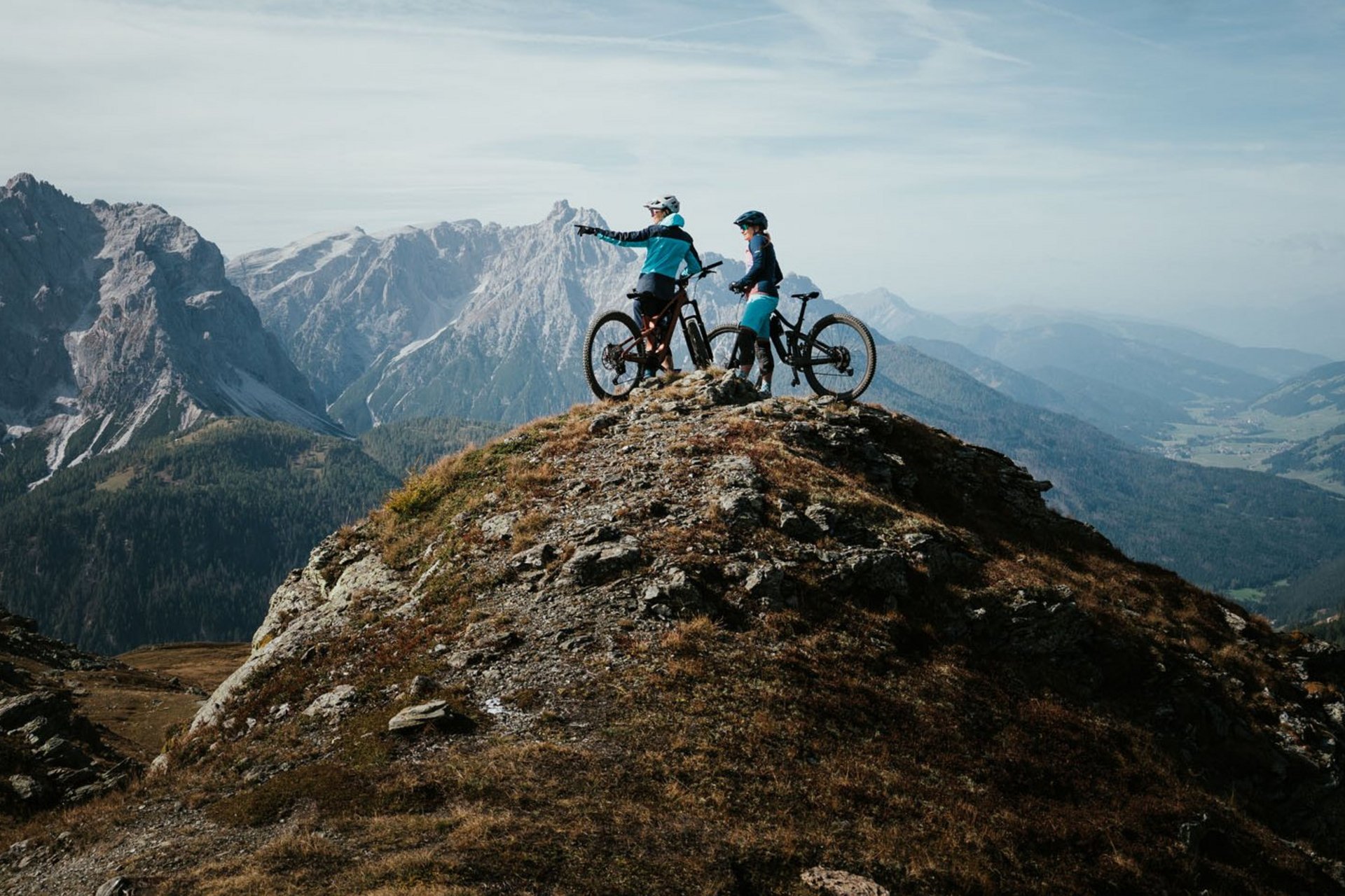 Zwei Mountainbiker auf einem Berggipfel mit Ausblick auf Gebirge