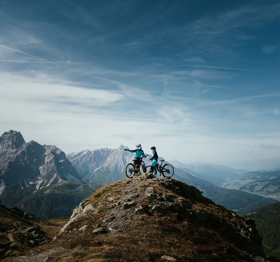 Zwei Mountainbiker auf einem Berggipfel mit Ausblick auf Gebirge