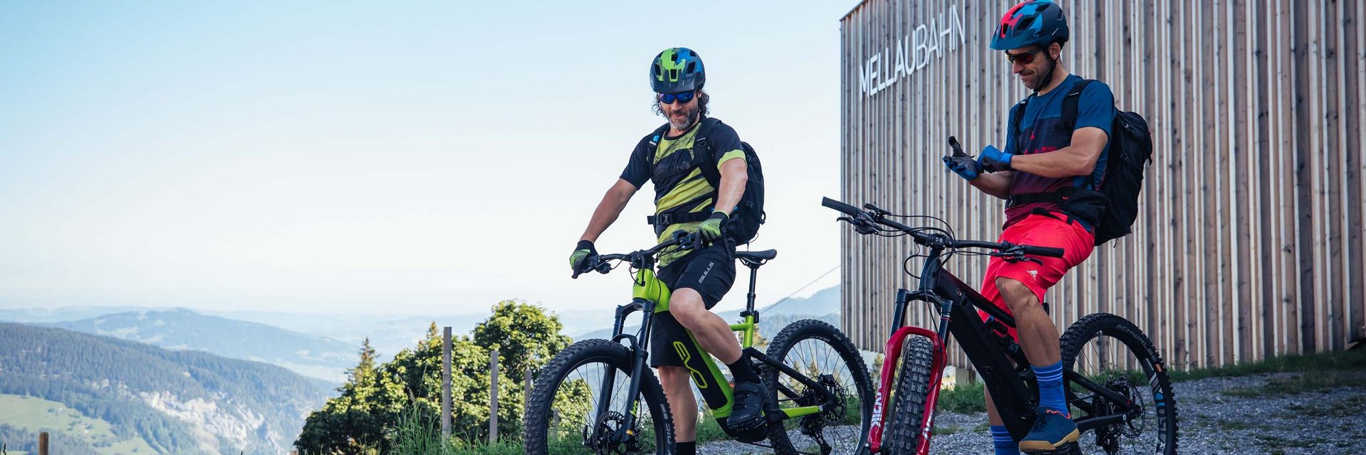 Twee mountainbikers met helmen bij het MellauBahn-gebouw in de bergen
