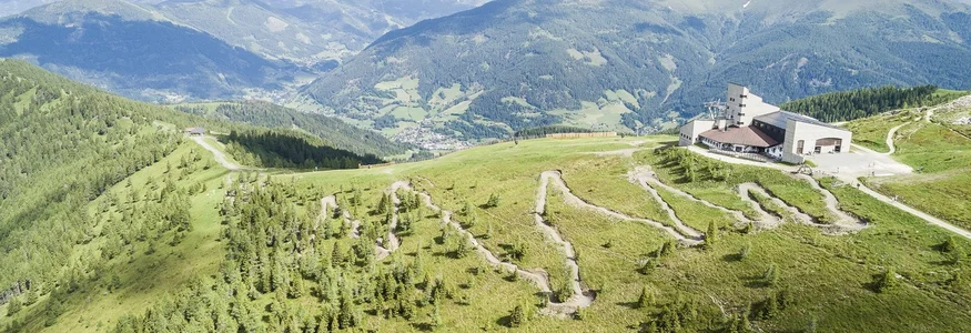 Luftaufnahme einer Bergstation mit Serpentinen und Alpenpanorama