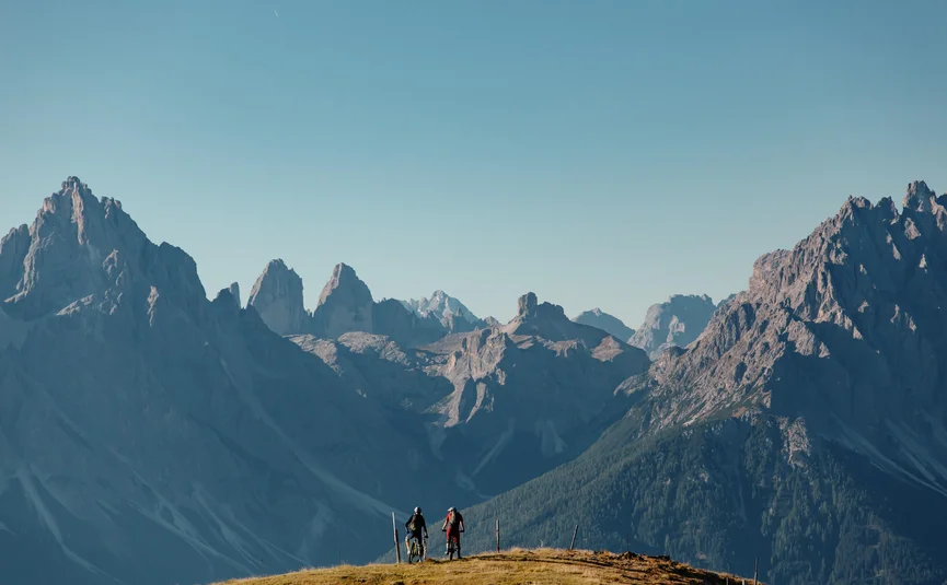 Twee fietsers op heuvel met uitzicht op hoge bergtoppen en blauwe lucht