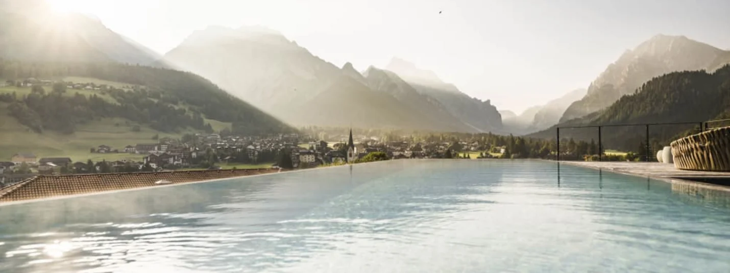 Infinity pool overlooking mountains and village in sunlight
