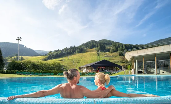 Couple relaxing in outdoor pool with mountain view and blue sky