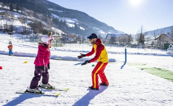 Family Ski & Ice Weeks Ski instructor teaching child to ski on sunny snowy mountain slope