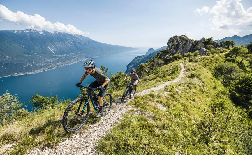 Two mountain bikers riding on a trail above a lake